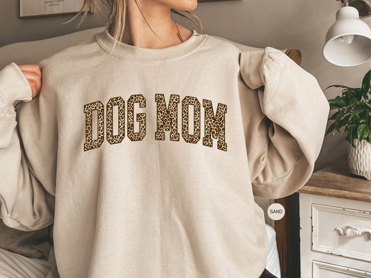 Sand colored Dog Mom varsity sweatshirt with leopard print lettering styled in cozy home setting