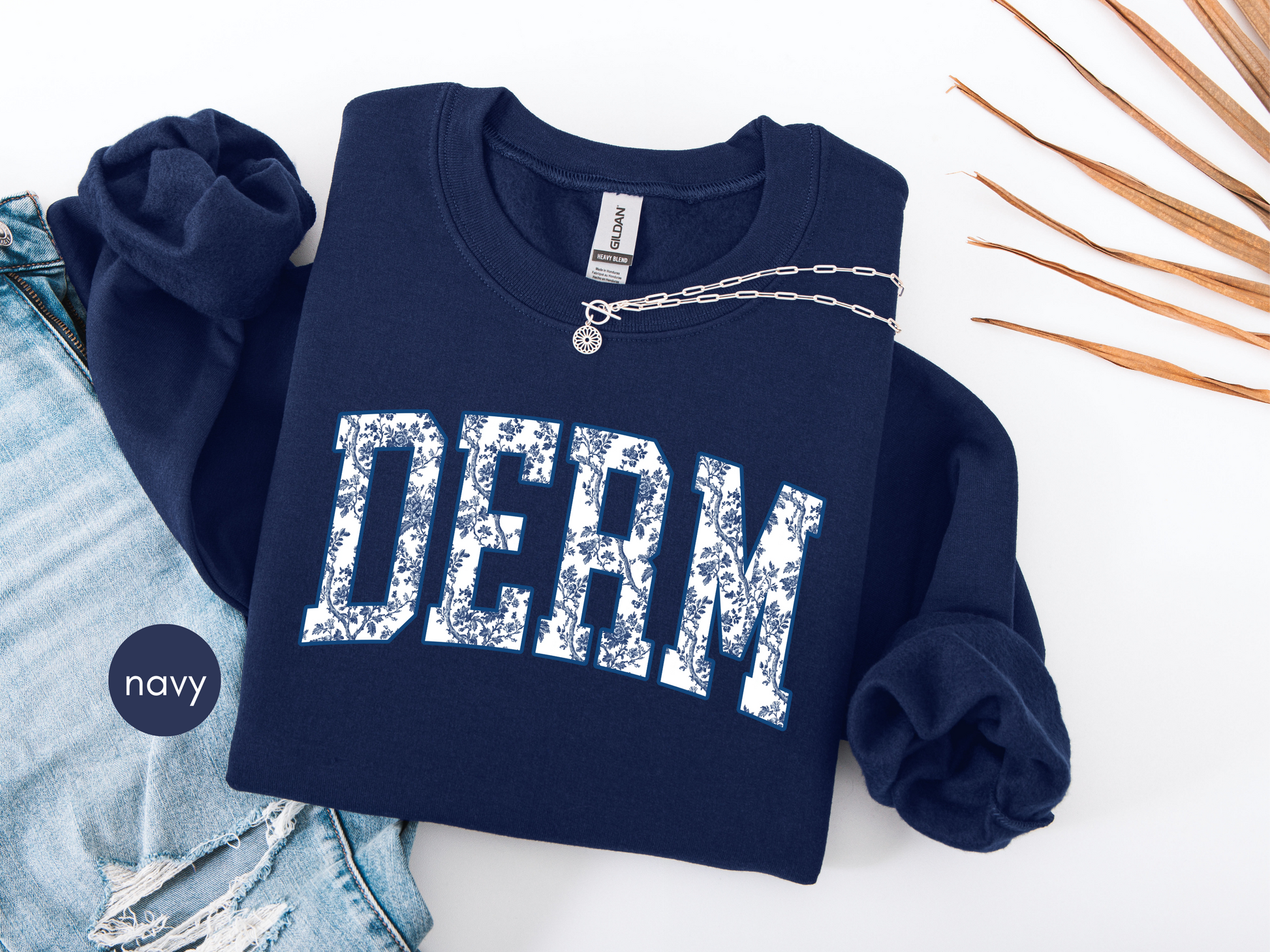 Navy blue DERM sweatshirt with blue toile lettering, flat lay styled as a dermatology nurse gift