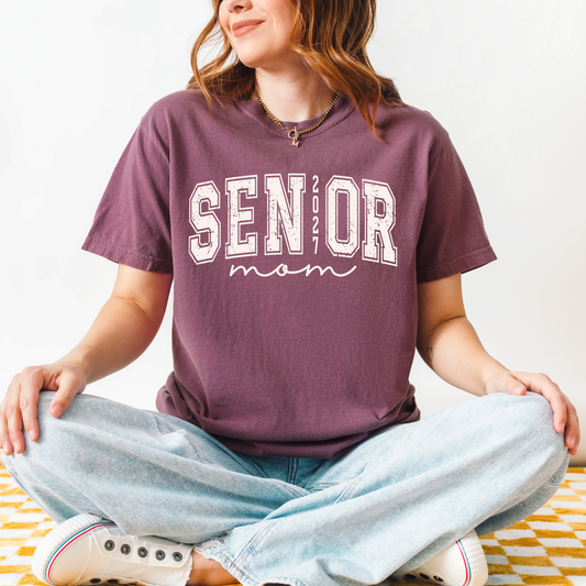 Senior Mom 2027 varsity graphic t-shirt on Comfort Colors garment-dyed tee for proud Class of 2027 moms attending football games, Senior Night, and graduation.