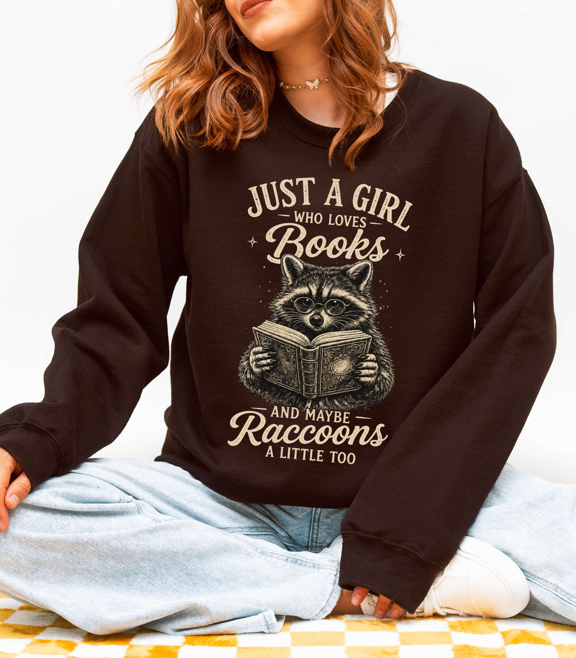 Woman wearing a chocolate book lover sweatshirt featuring a vintage raccoon reading and the phrase Just a Girl Who Loves Books and Maybe Raccoons a Little Too.