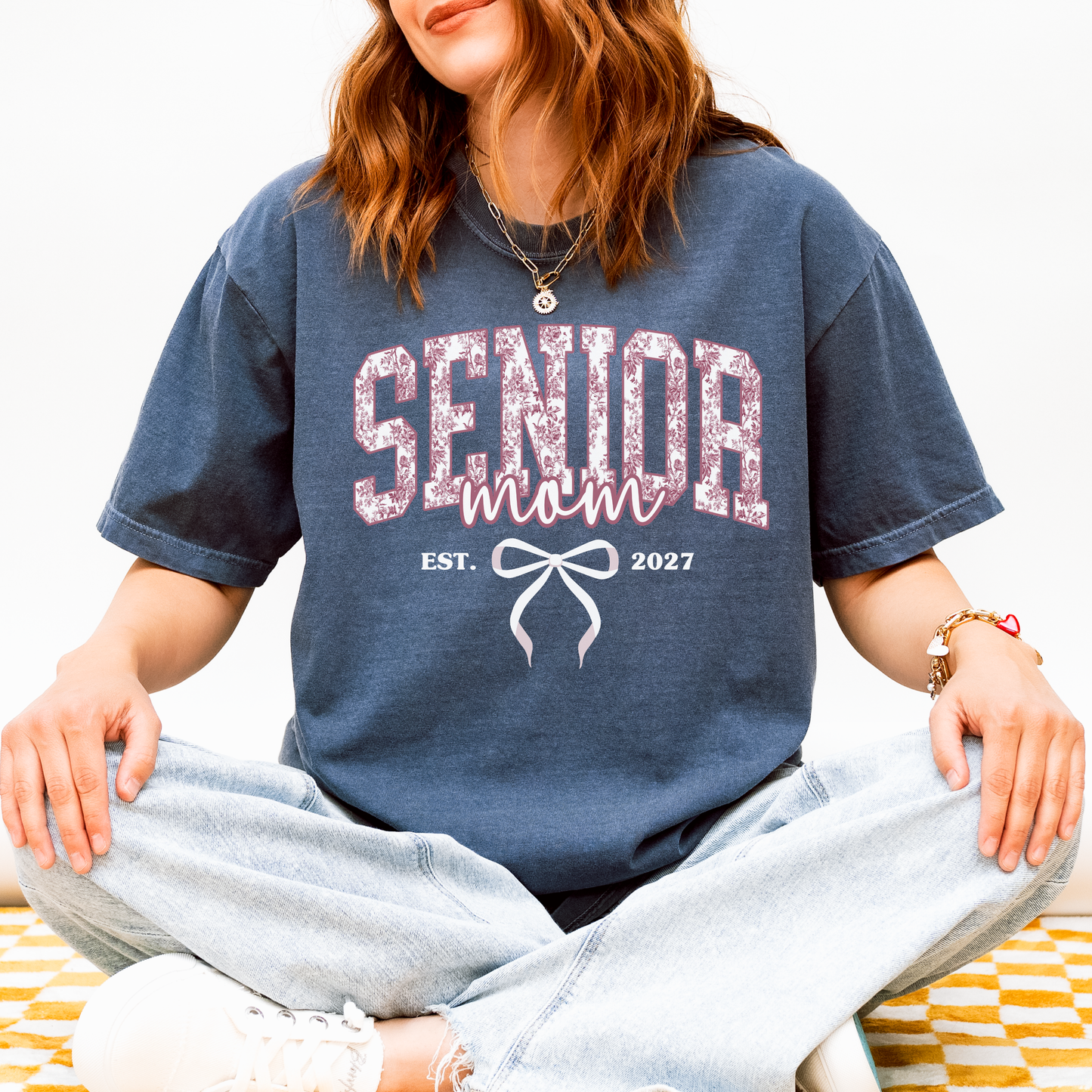 Senior Mom Est. 2027 Comfort Colors navy blue shirt featuring a pink toile varsity design with bow, perfect for Class of 2027 graduation celebrations and senior moms.