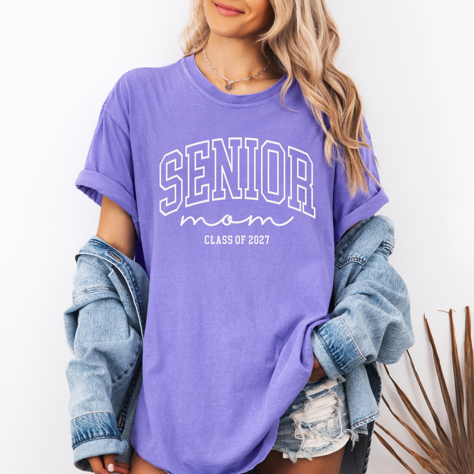 Purple Comfort Colors® Senior Mom Class of 2027 graphic t-shirt featuring a varsity-inspired design for proud moms celebrating senior year and graduation.
